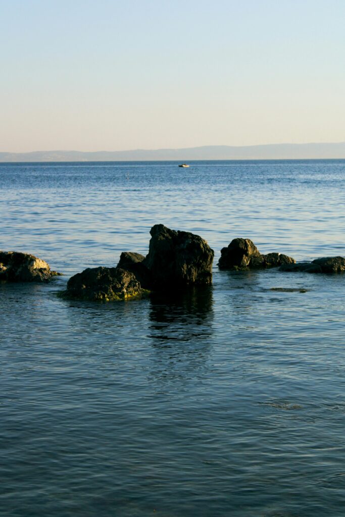 Pedras no mar com horizonte distante, representando sonhar com água e desafios emocionais.