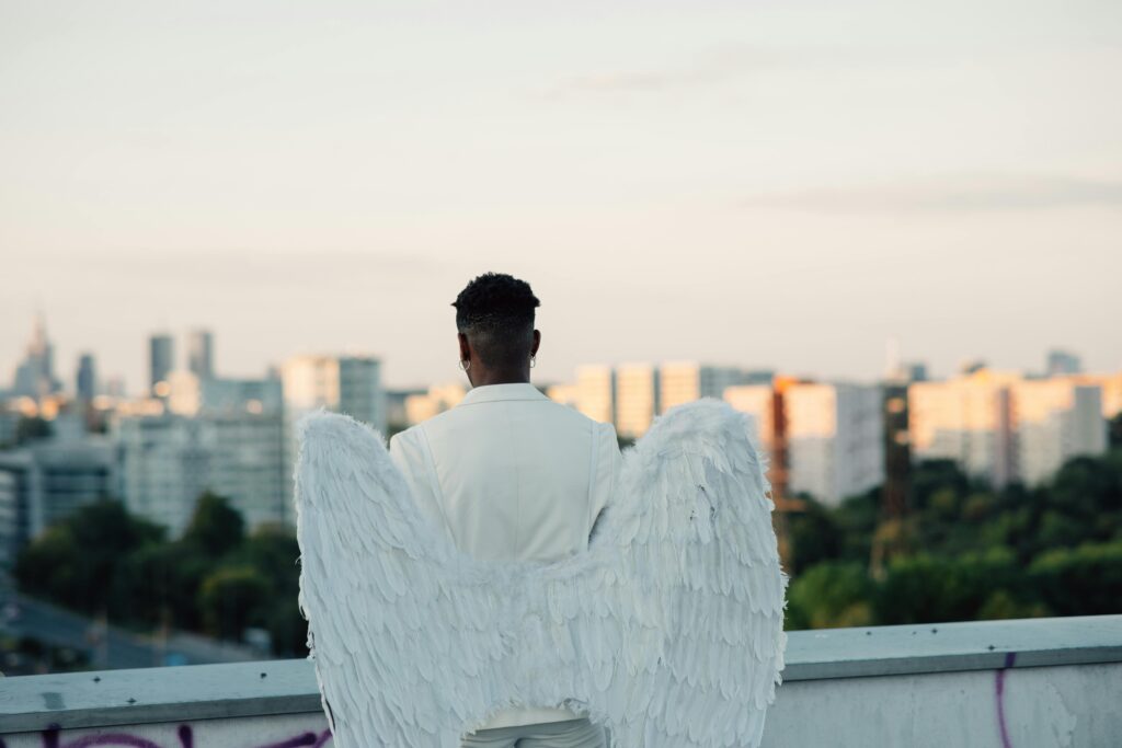 pessoa com asas de anjo brancas olhando para a cidade ao pôr do sol