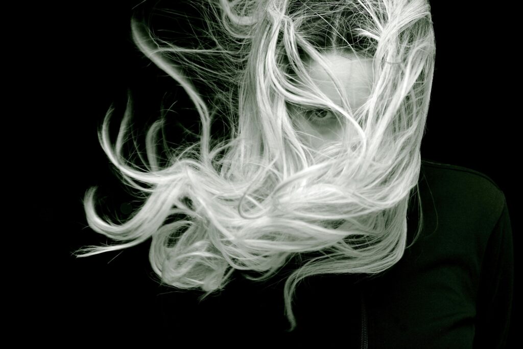 Mulher com cabelo claro esvoaçante cobrindo parcialmente o rosto, simbolizando mistério e inseguranças nos sonhos.