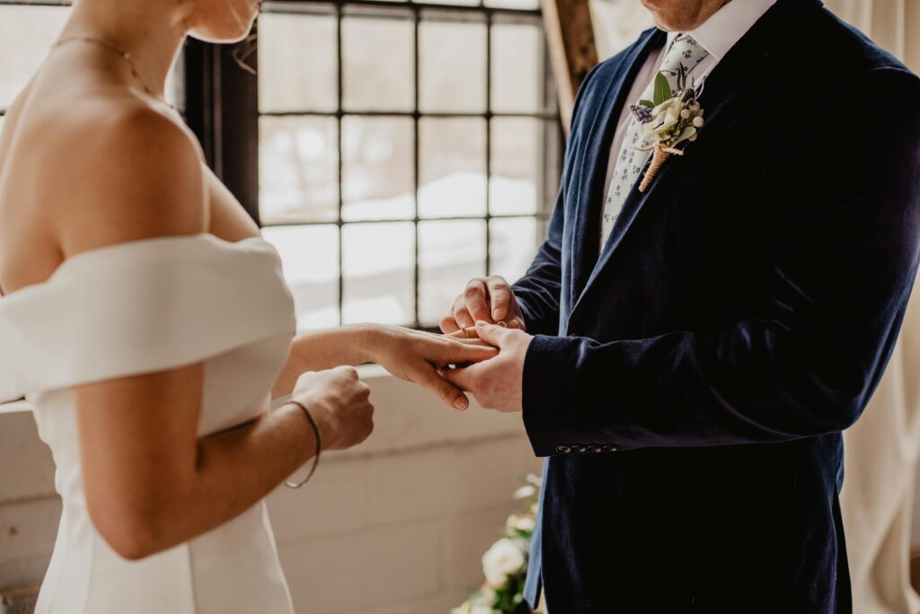 Noivo colocando aliança na noiva em casamento intimista, representando sonhos de novos começos.