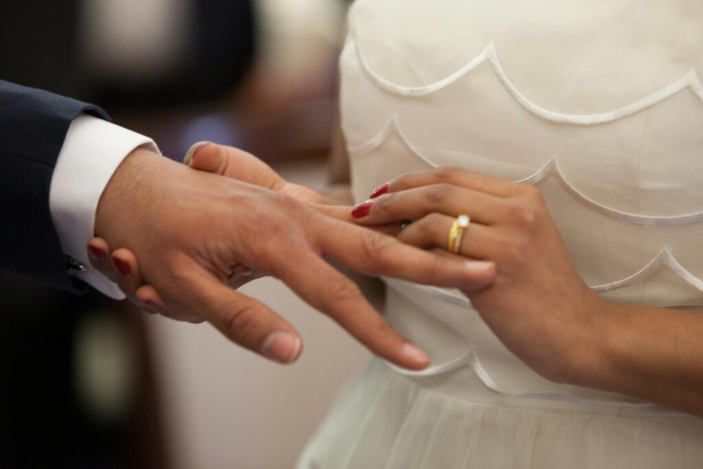 Mulher colocando aliança na mão do noivo durante cerimônia de casamento, simbolizando sonhos com união e compromisso.