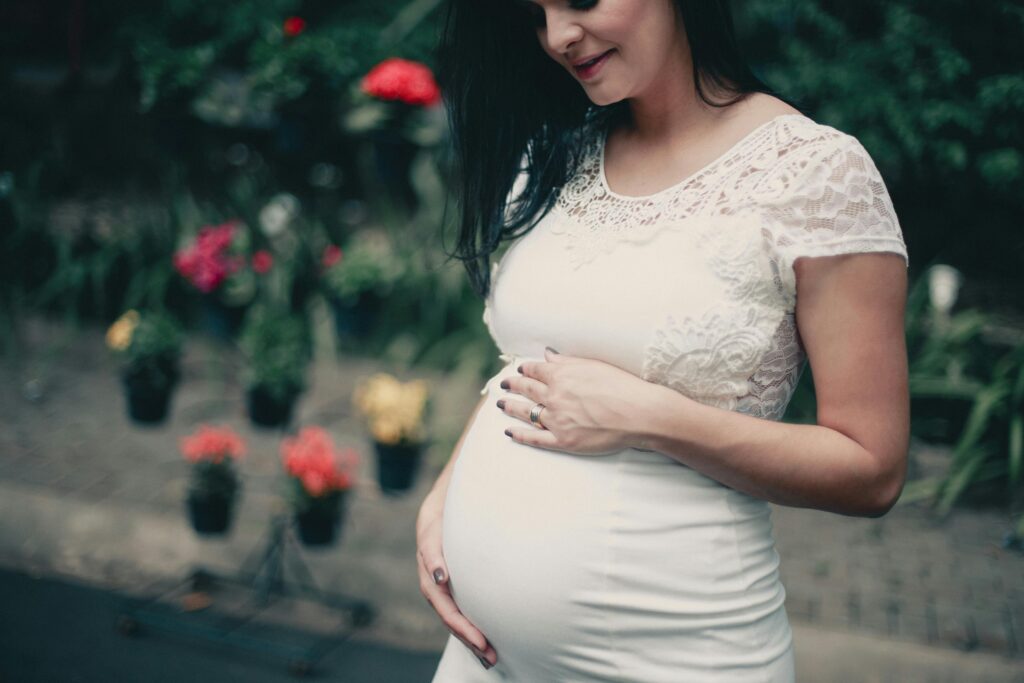 Mulher grávida de vestido branco tocando a barriga, transmitindo pureza, esperança e novos significados em sonhos.