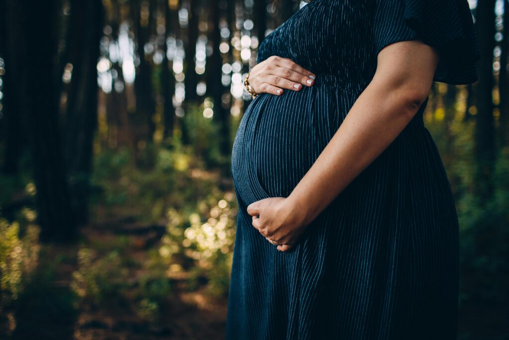 Mulher grávida em ambiente natural, segurando a barriga como símbolo de renovação e fertilidade nos sonhos.
