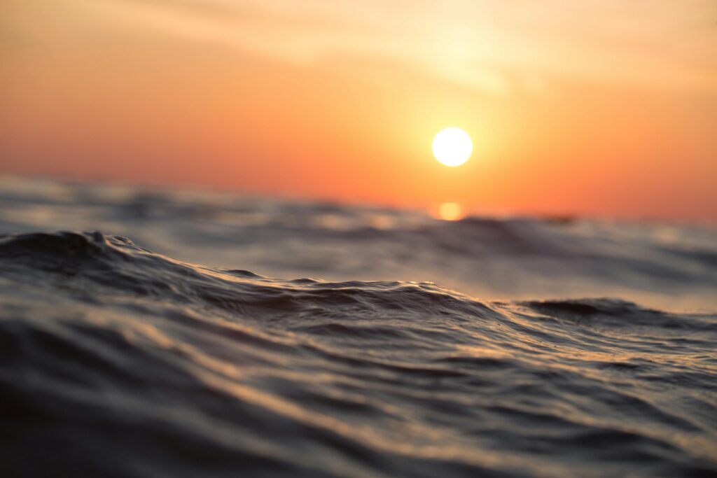 Ondas do mar em primeiro plano com sol se pondo no horizonte.