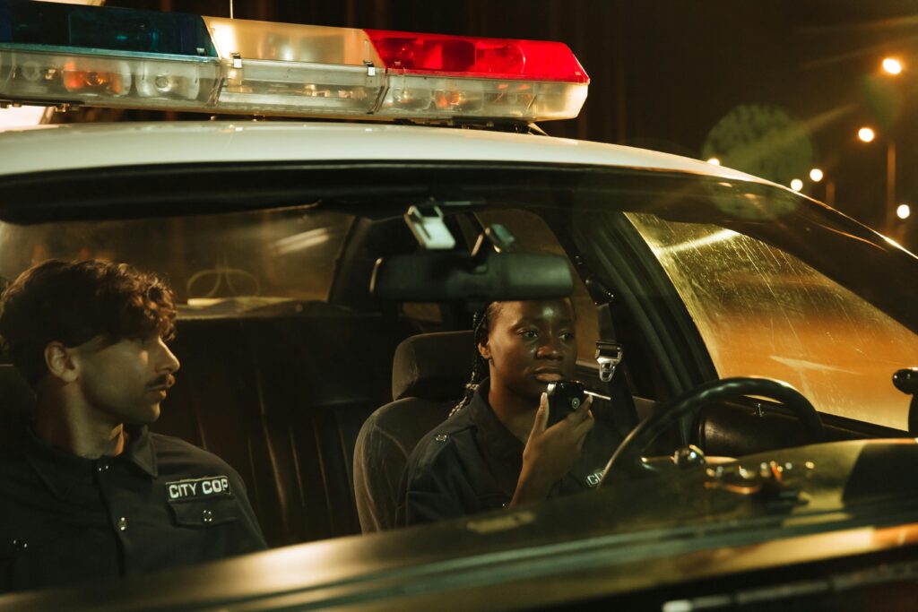 Policiais em viatura à noite, comunicando-se pelo rádio, simbolizando vigilância e autoridade.