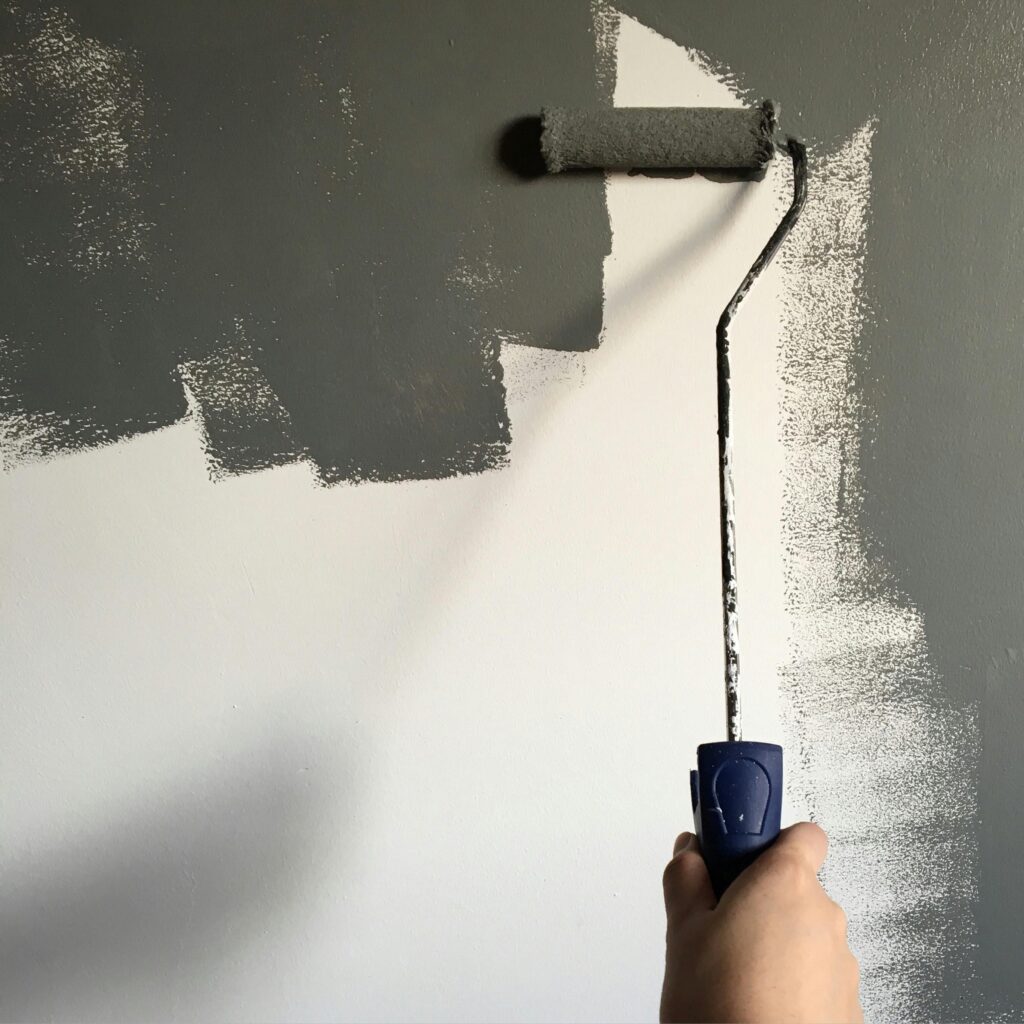 Pessoa pintando parede de cinza durante uma reforma, representando o simbolismo de sonhar com reforma de casa.