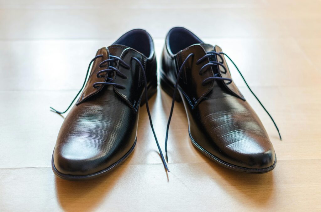 Sapatos sociais pretos de couro sobre piso de madeira, refletindo elegância e status.