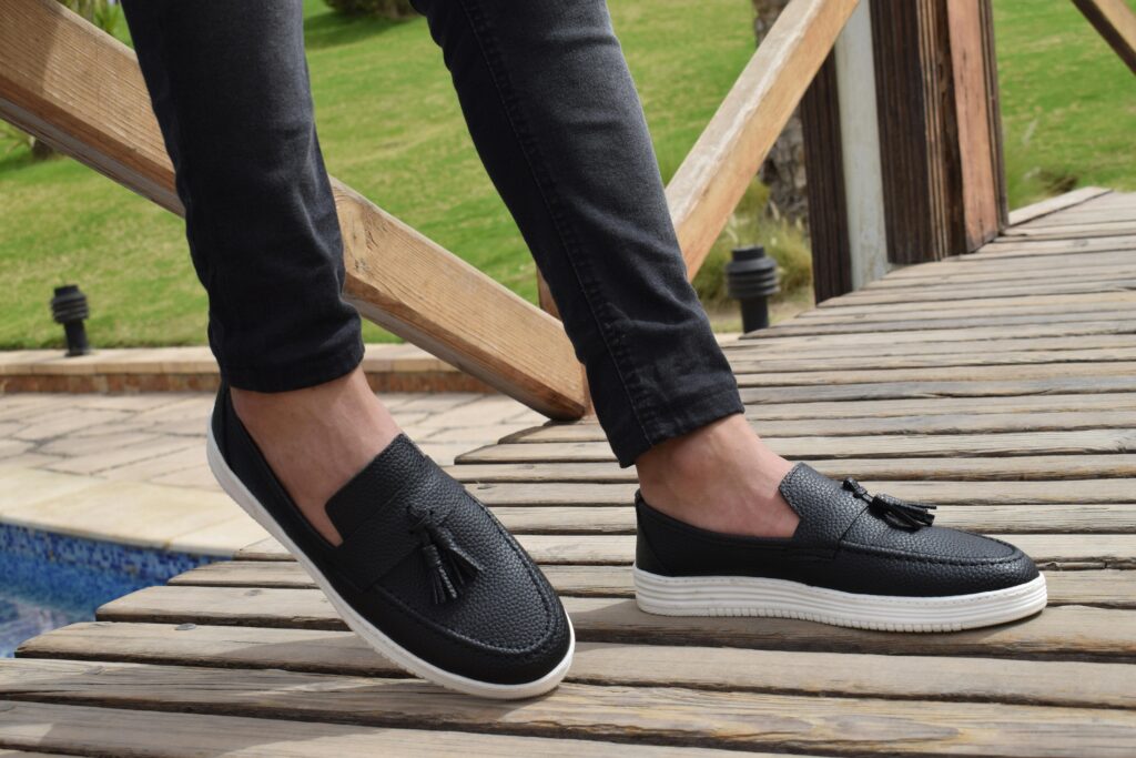 Pessoa usando sapatos pretos sociais com tassels em ponte de madeira, conceito de sonhar com sapatos elegantes.
