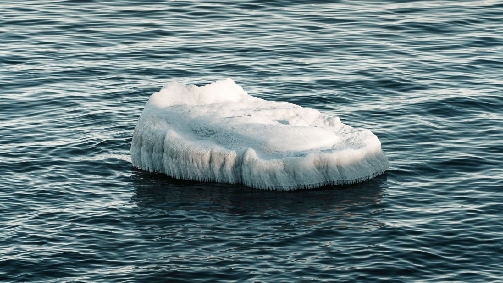 Imagem horizontal de um enorme iceberg flutuando em um mar calmo ao entardecer